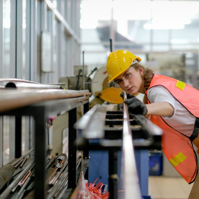 Factory technician or worker woman with safety uniform hold copper tube and look to camera in manufacture workplace. Concept of good management for industrial business with professional employee.