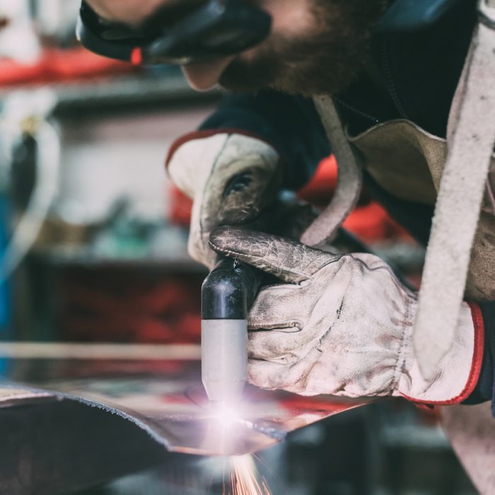 Metalworker plasma-cutting copper in forge workshop